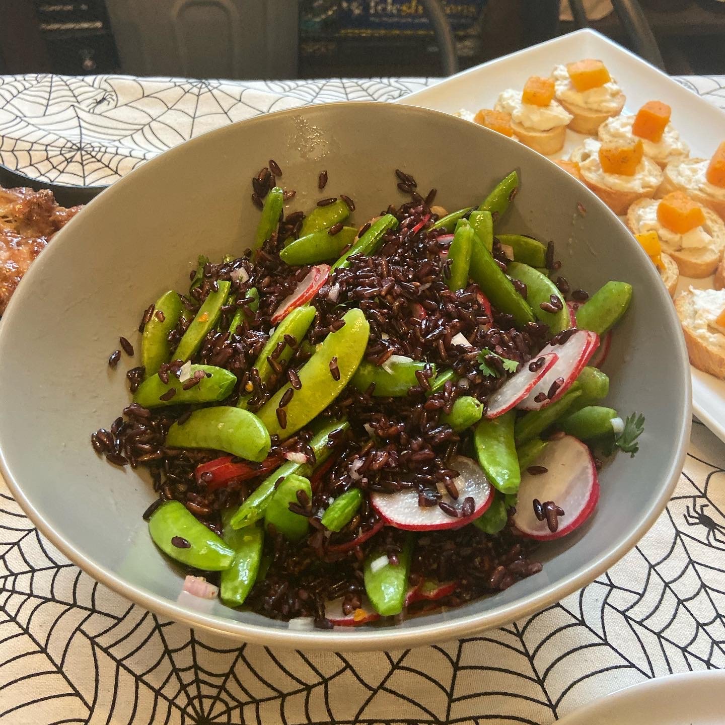 This is a bowl of rice salad, with black rice, radishes, and snap peas.