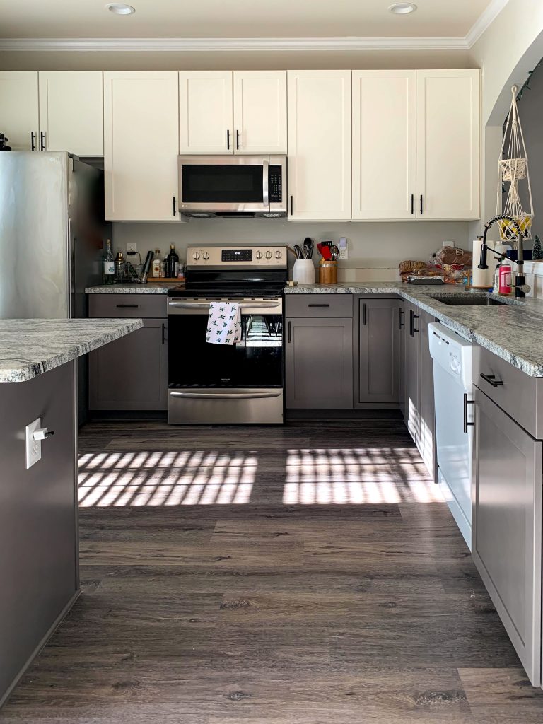 This is a two-toned kitchen with Shaker cabinets, with cream upper cabinets and gray lower cabinets. It has had some appliances replaced during the renovation process.