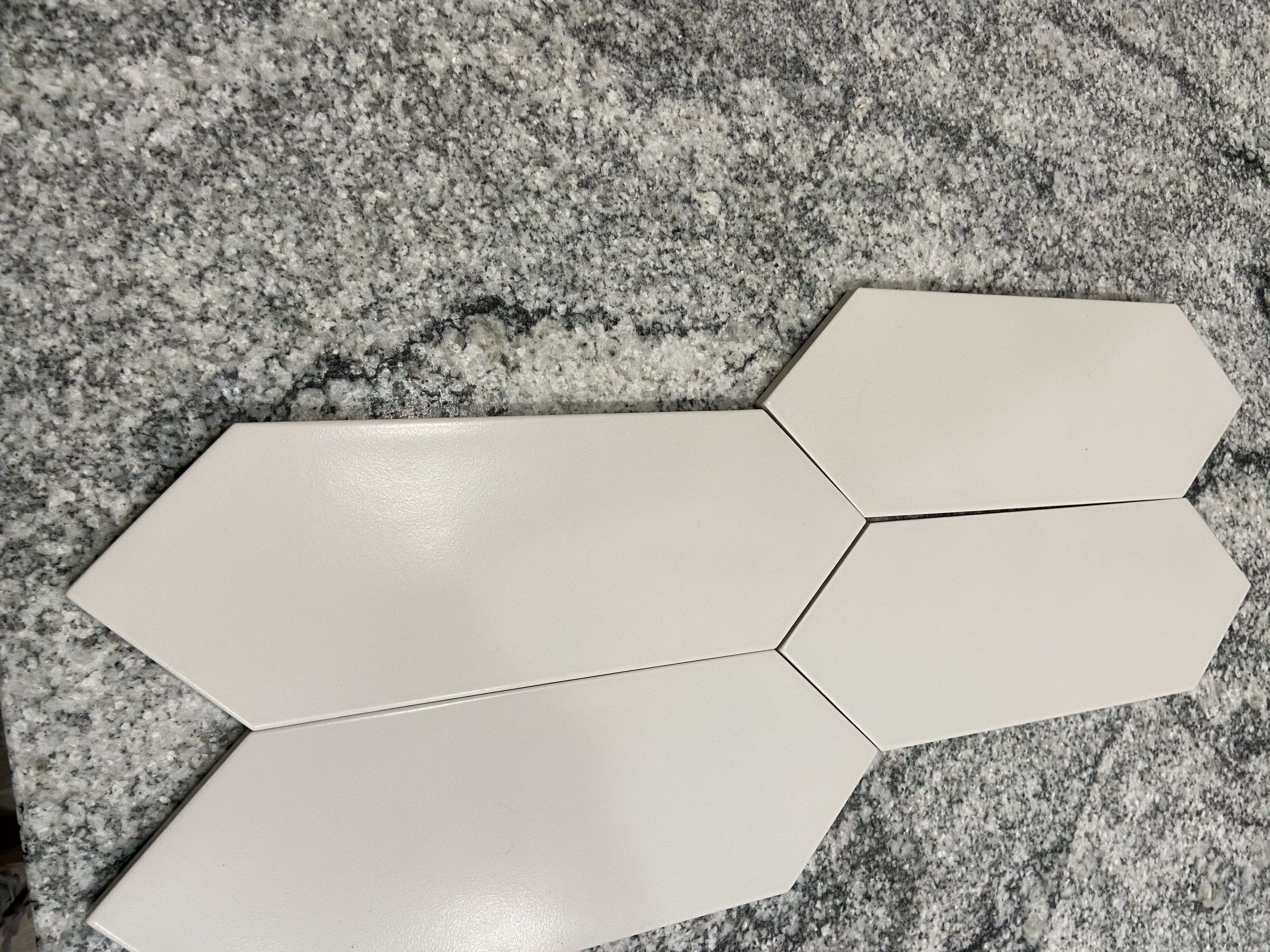 These are four off-white picket-shaped tiles lying on a variegated granite counter.