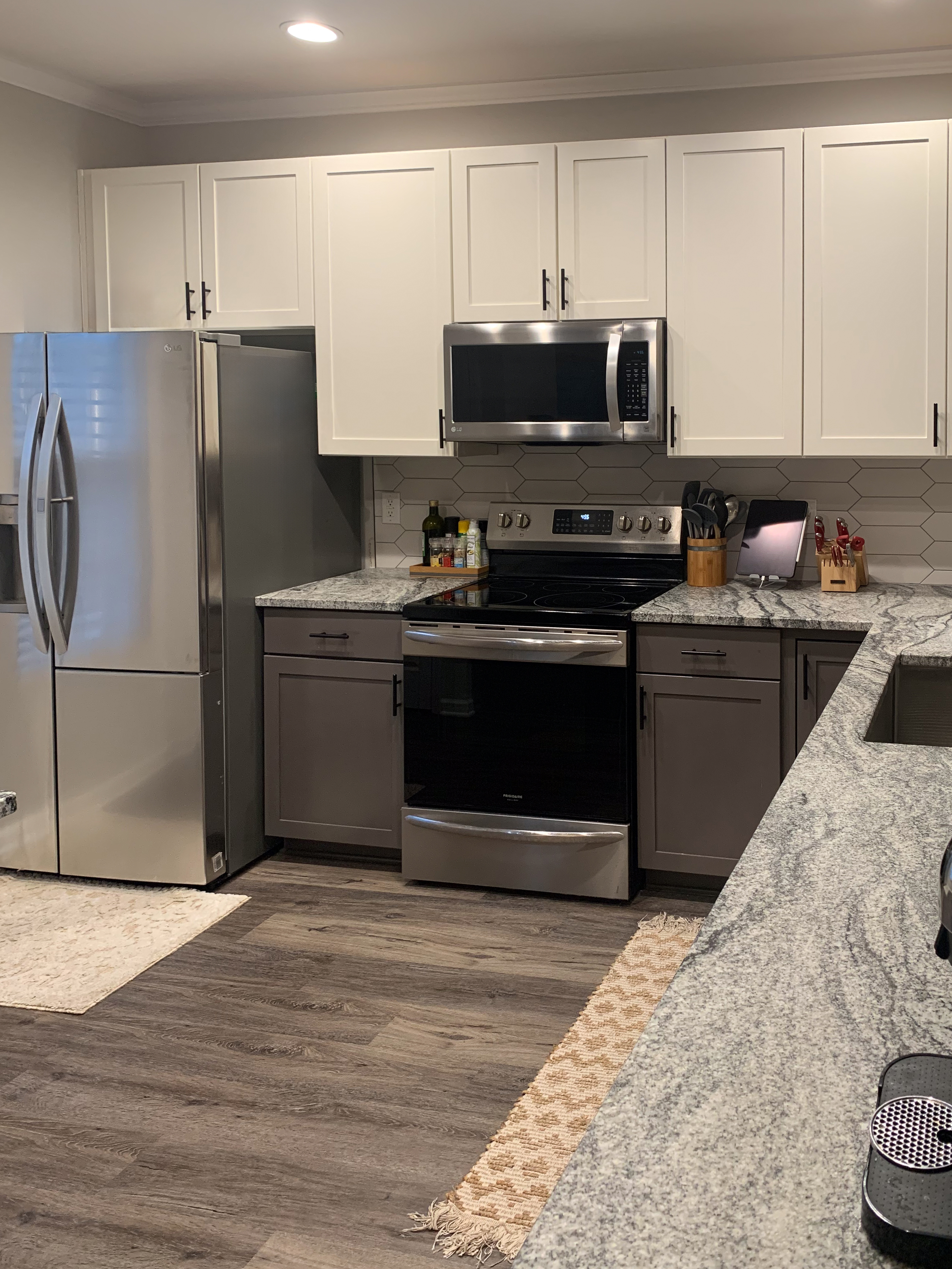 This is a Shaker-style kitchen, with a view that just includes the peninsula in the bottom left. The cabinets are off-white on the top and a deep greige on the bottom.