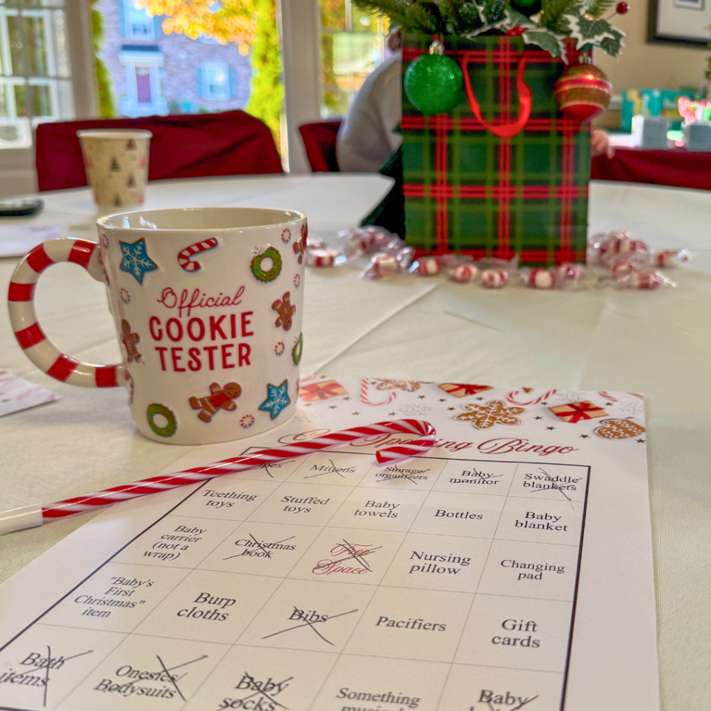 Baby shower table with a mug reading 'Official Cookie Tester,' candy cane pen, a festive Baby Shower Bingo card, and a plaid gift bag centerpiece.