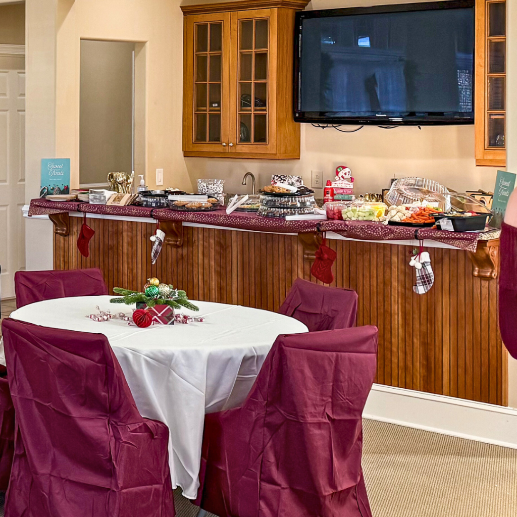Christmas buffet table setup with red and gold accents, a variety of food platters, stockings hanging from the counter, and a small centerpiece featuring evergreen sprigs and ornaments.